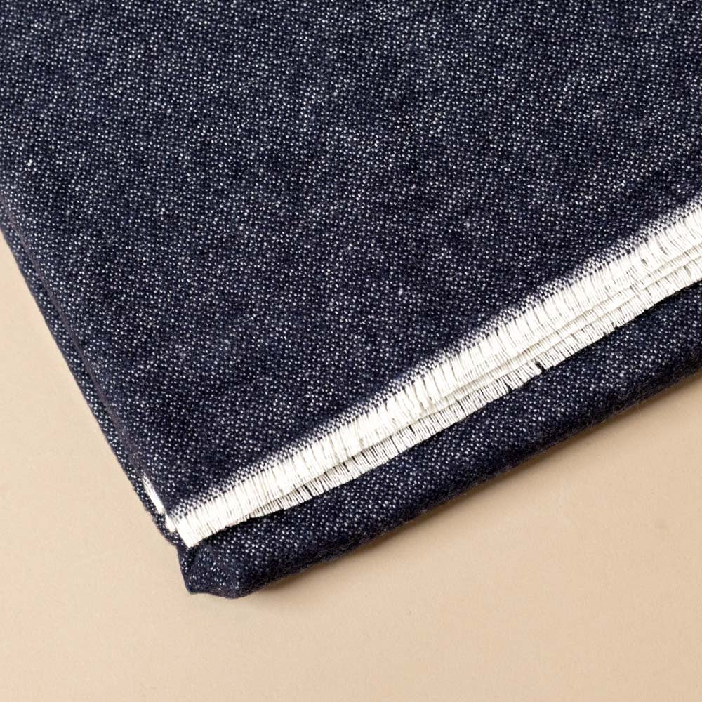 aspen-throw-navy Close-up of dark denim colored fabric with a white stripe on a beige background