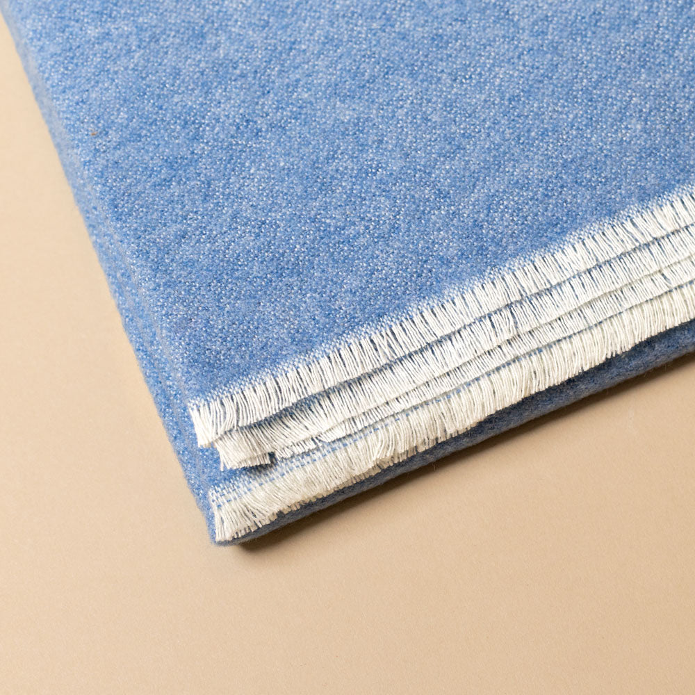 aspen-throw-niagra Close-up of blue with white fringe on a beige background