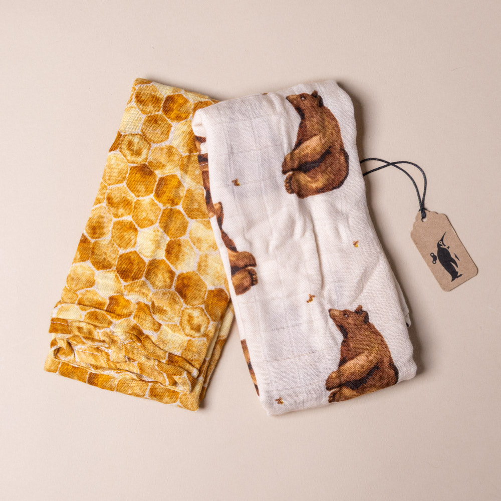 bamboo-burpie-set-honey-bear Two baby burpies, one with honeycomb pattern and the other with bear design, on a beige background.