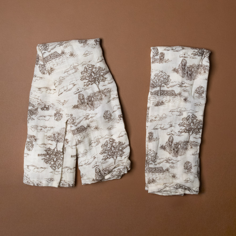 bamboo-burpie-set-meadow-toile Two folded fabric burpies with a nature-themed pattern on a brown background