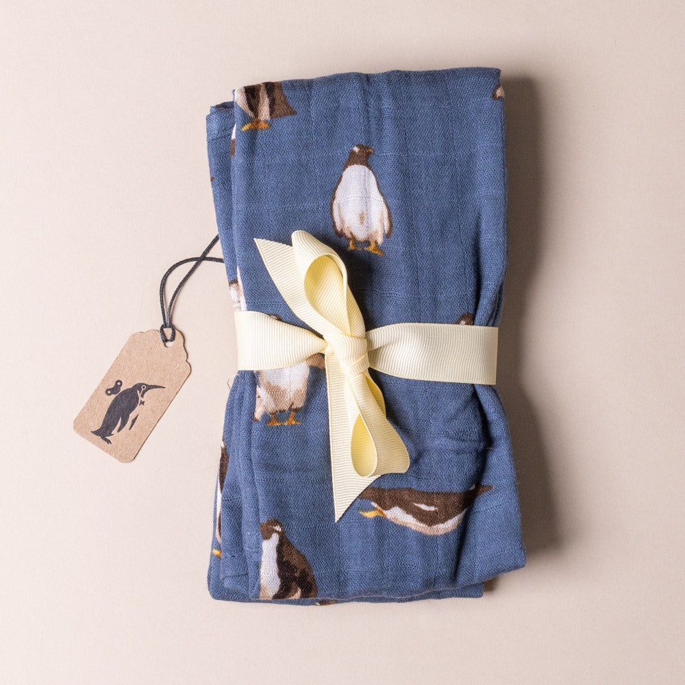 bamboo-burpie-set-penguins Folded blue fabric with penguin pattern and a yellow ribbon on a beige background