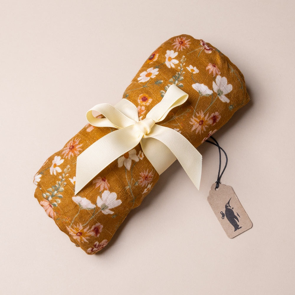 bamboo-swaddle-wildflower Floral-patterned blanket with a white ribbon on a beige background