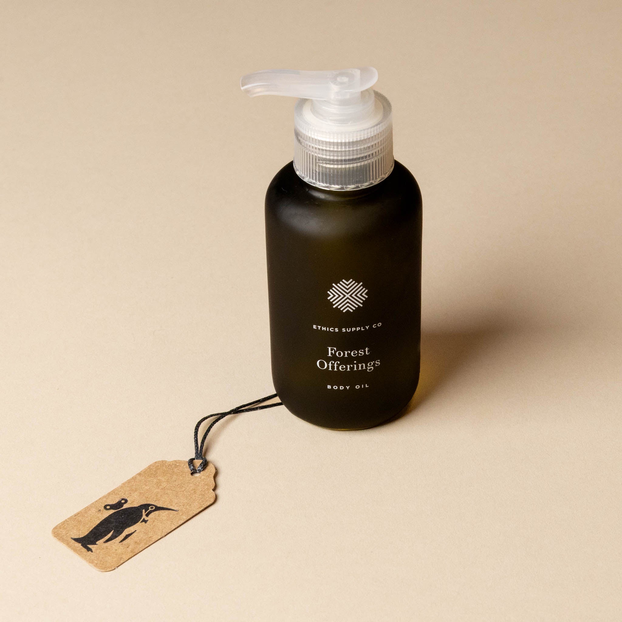 Black bottle of 'Forest Offering' body oil with a pump on a beige background, featuring a branded tag.