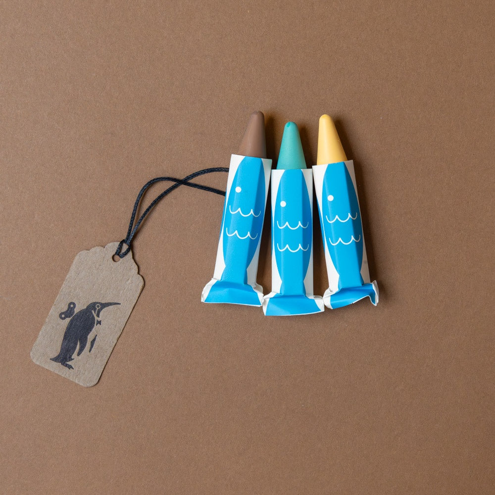 buttery-soft-rice-wax-bath-crayons--3pc-turtle Three blue fish-shaped crayons with a brown tag on a brown background