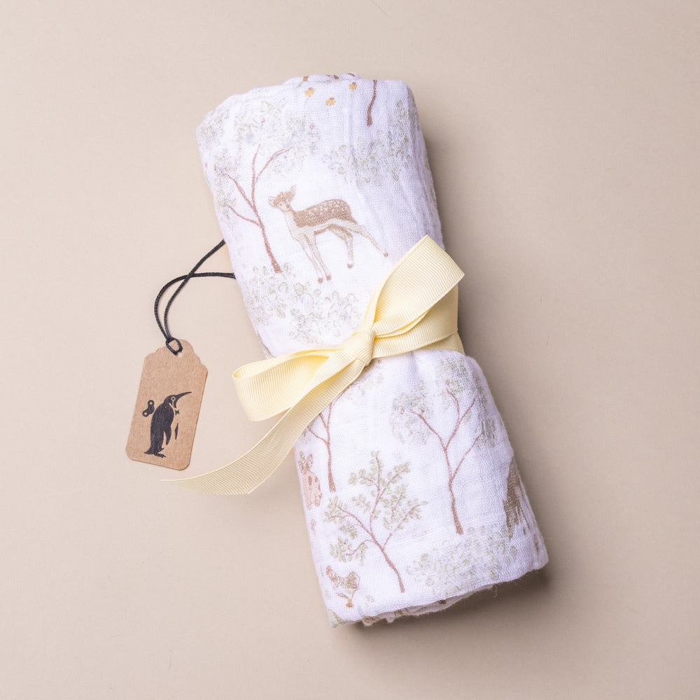 cotton-muslin-swaddle-woodland-friends Folded fabric with deer design and yellow ribbon on a beige background