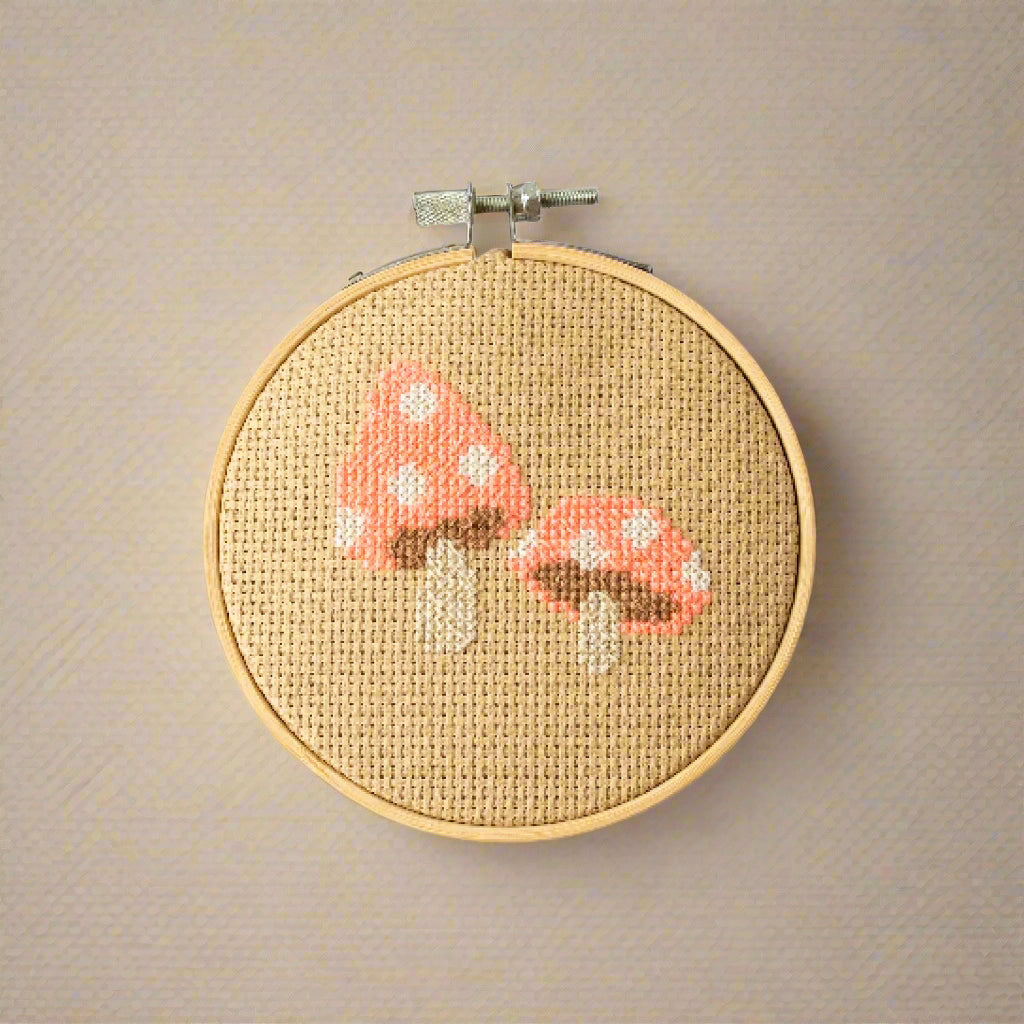 Cross-stitched mushrooms on a wooden hoop with a white background