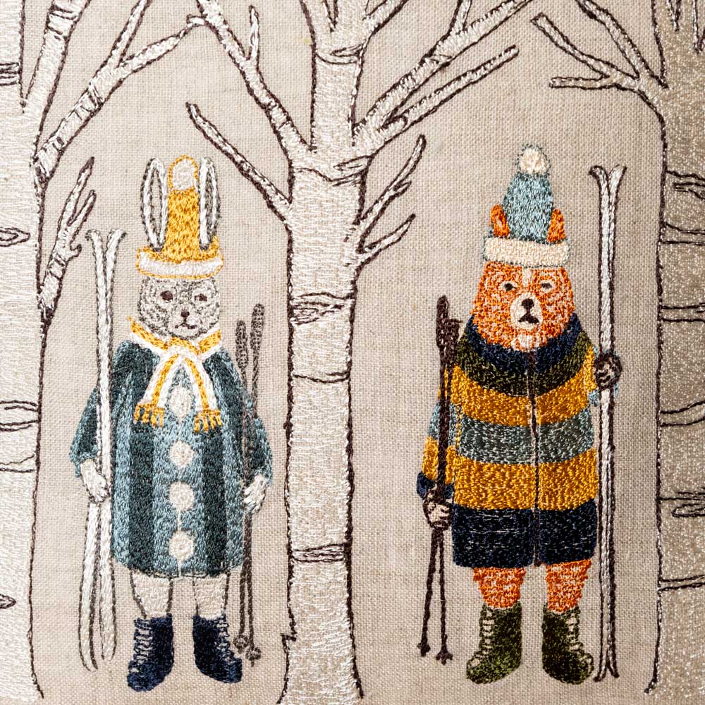 embroidered-pillow-aspen-skiers of a bear and a rabbit in winter clothing with skis against a tree background.