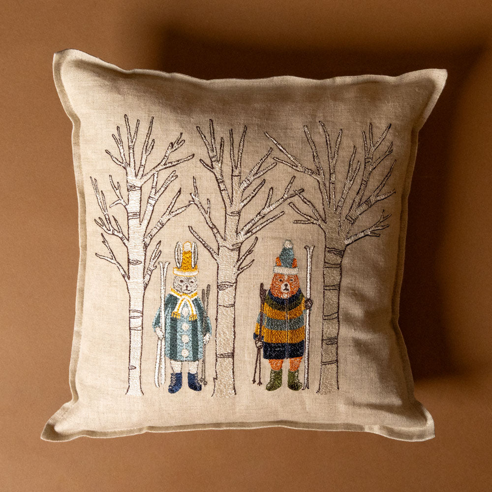 embroidered-pillow-aspen-skiers with embroidered bears in winter clothing and trees on a brown background