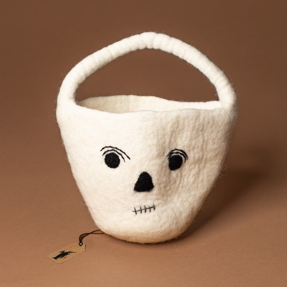 felt-skeleton-bucket White skull-shaped basket with black facial features on a brown background