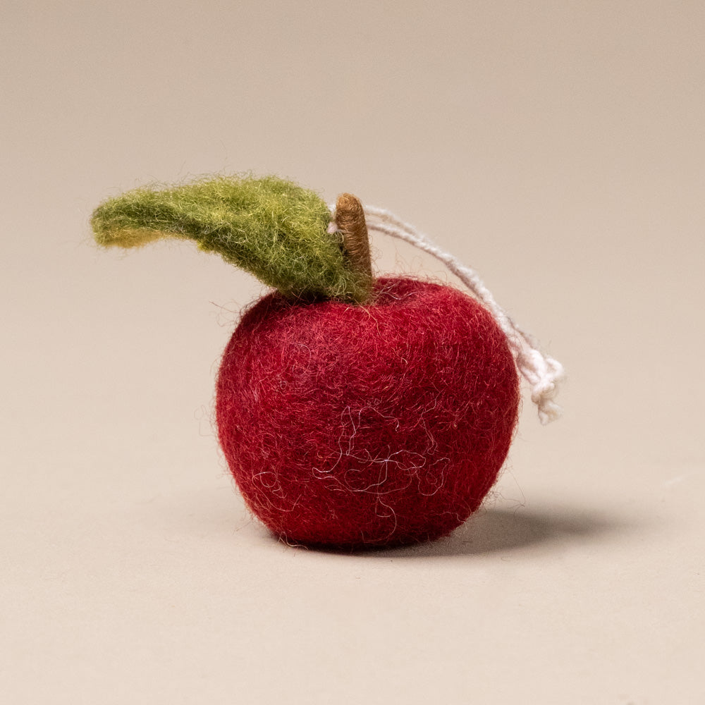 felted-apple-ornament-ruby-red Red felt apple ornament with a green leaf on a beige background