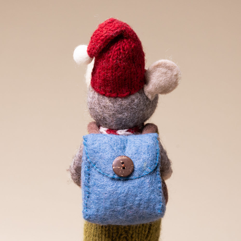 felted-grey-mouse-green-overalls-and-back-pack Small stuffed mouse wearing a red knitted hat and blue knitted vest on a beige background