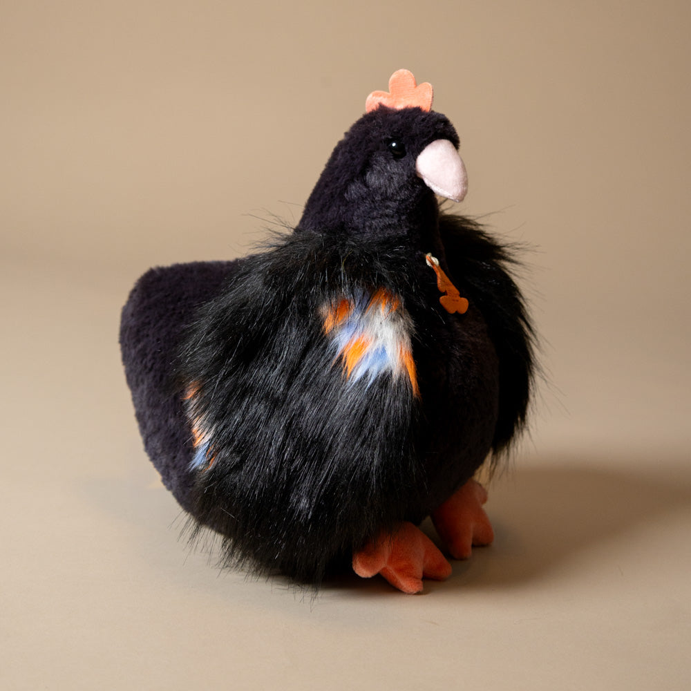Plush toy floofy-chicken-black with black feathers, orange beak, and feet on a beige background