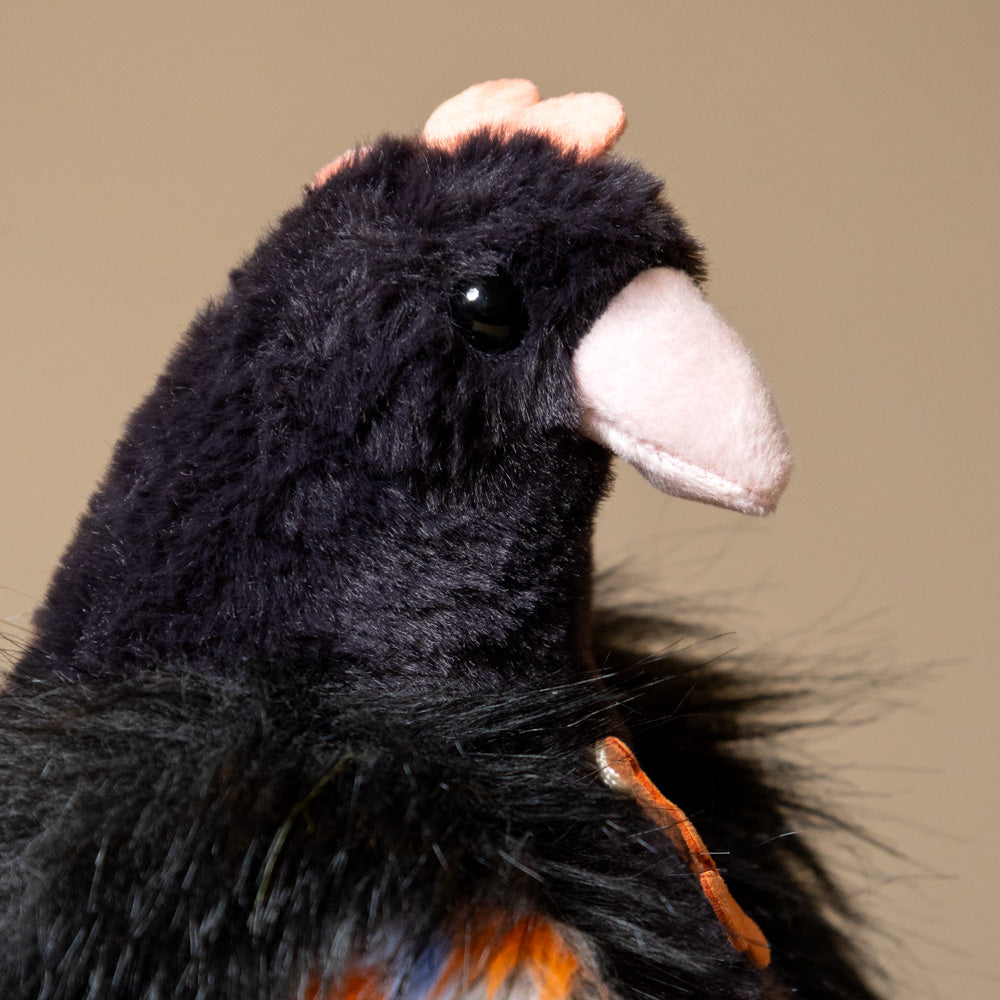Close-up of floofy-chicken-black plush toy with a brown background