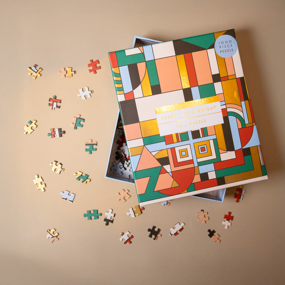 frank-lloyd-wright-1000m-piece-puzzle-december-gifts Colorful geometric-patterned puzzle box with scattered pieces on a beige background