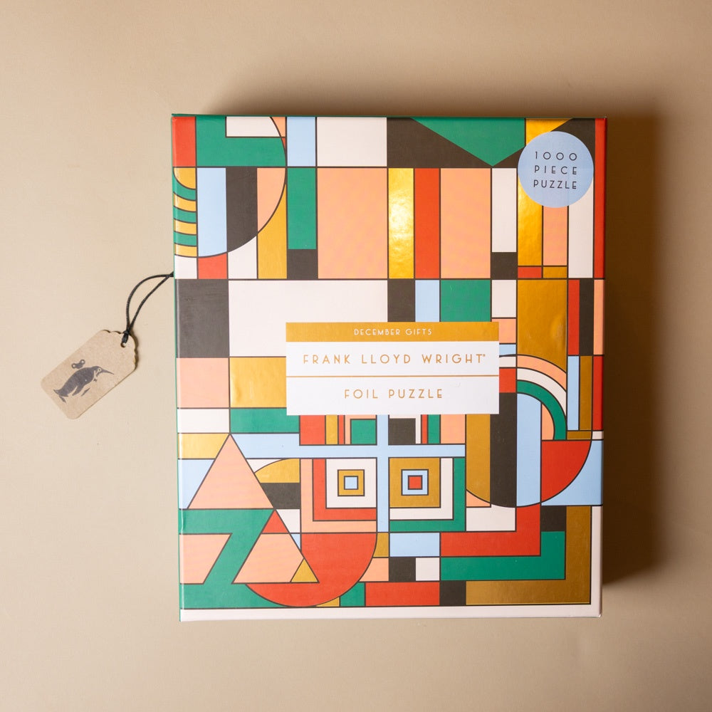 frank-lloyd-wright-1000m-piece-puzzle-december-gifts Colorful geometric-patterned puzzle box with a tag on a beige background