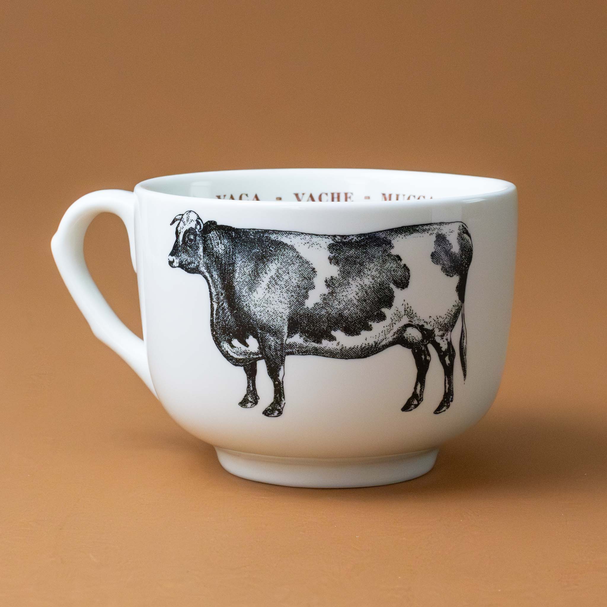 white-cup-grande-stoneware-cup-black-illustration-of-cow-with-the-word-cow-in-red-in-several-languages-on-interior