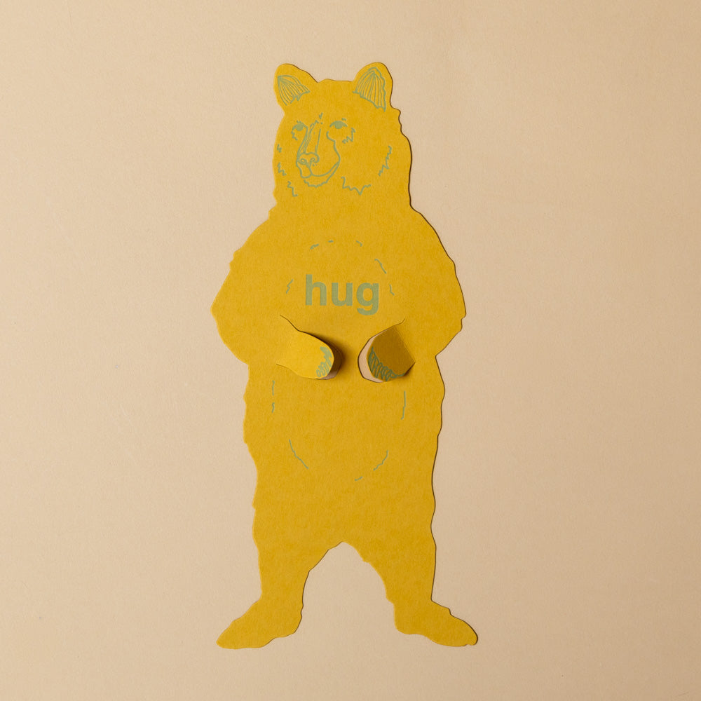 grizzly-bear-letterpress-gift-greeting-card Yellow bear-shaped object with 'hug' text on a beige background