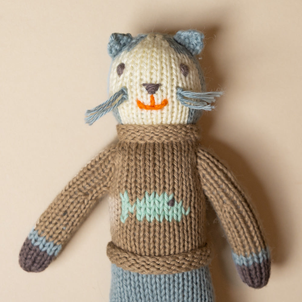 hand-knit-rattle-sardine-kitten with a brown body and blue accents on a beige background