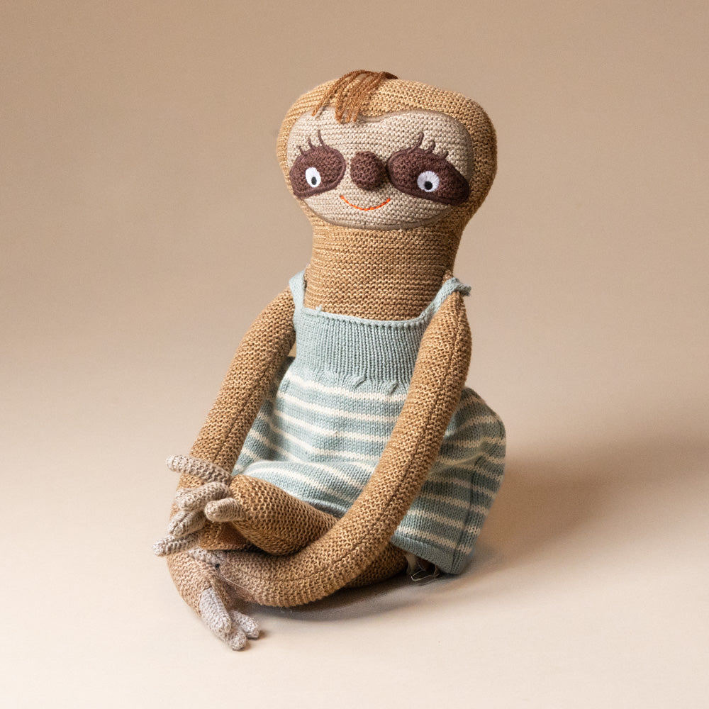 hanna-sloth Knitted sloth toy wearing a striped dress on a beige background