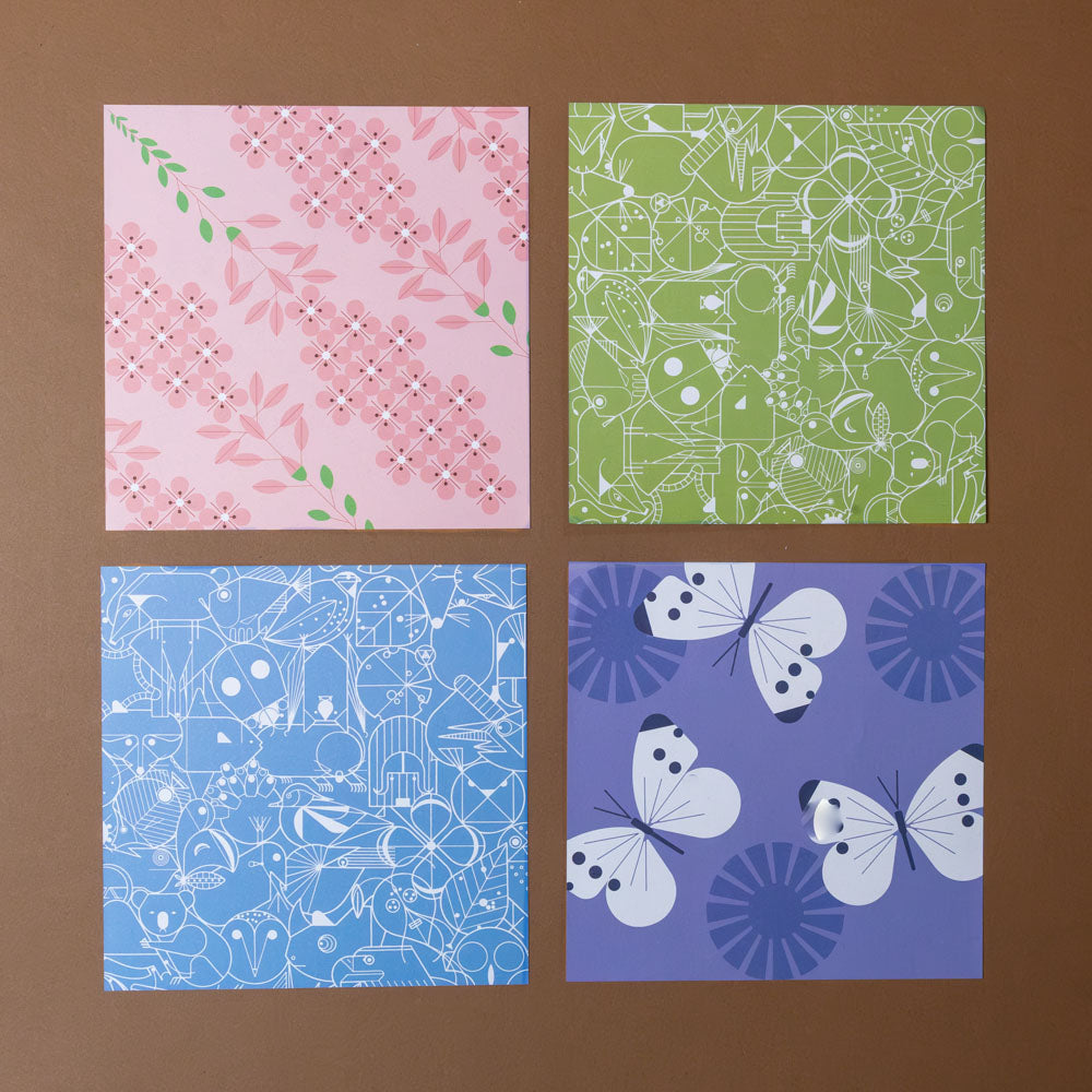 make-your-own-charley-harper-origami-animals-kit Four patterned paper sheets in pink, green, blue, and purple on a brown background