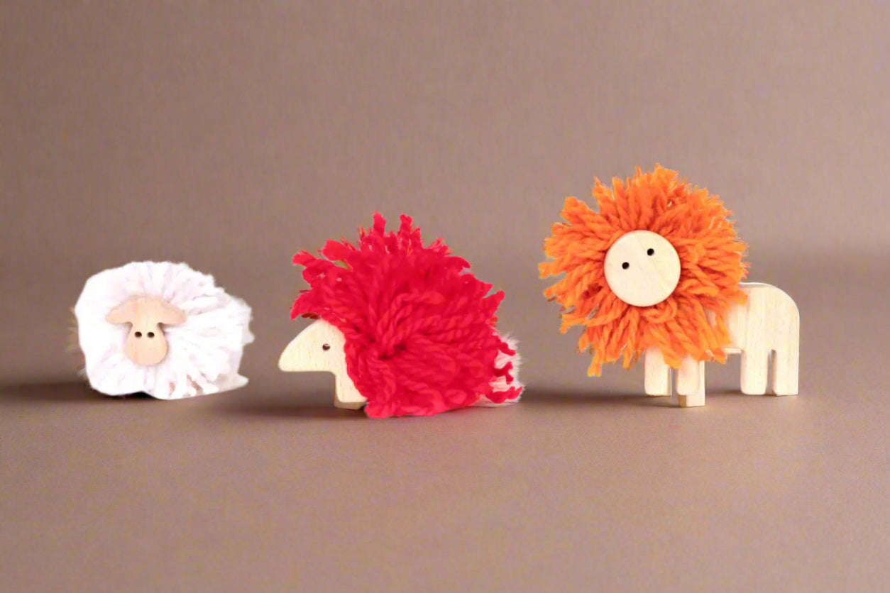Three colorful make-your-own-pom-pom-animal toys on a brown background