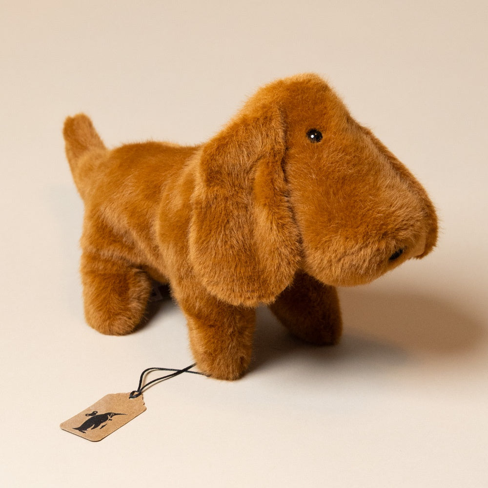 muzzle-dale-dachshund-pup-large Brown plush dog toy with a tag on a beige background