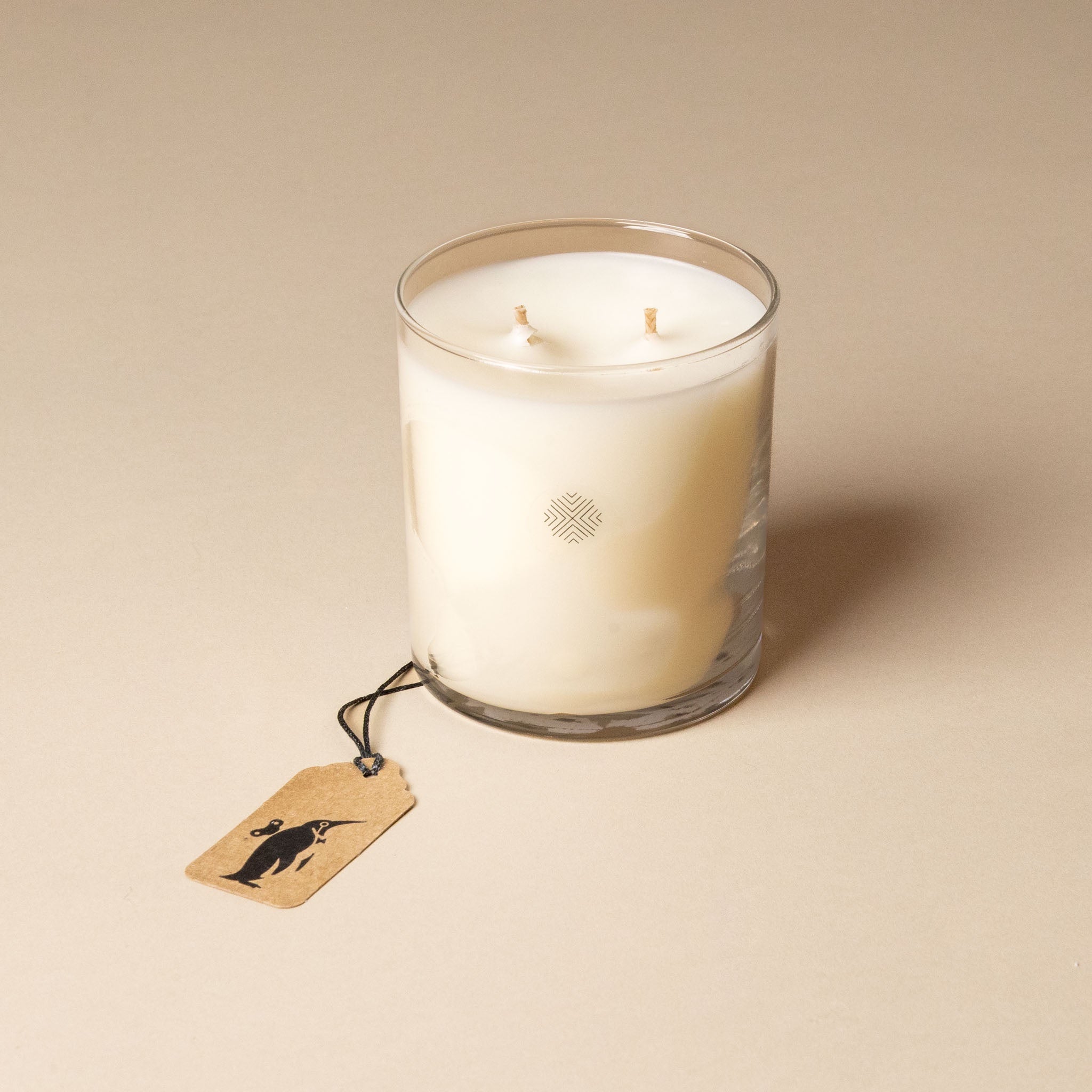 White candle in a glass jar with a tag on a beige background