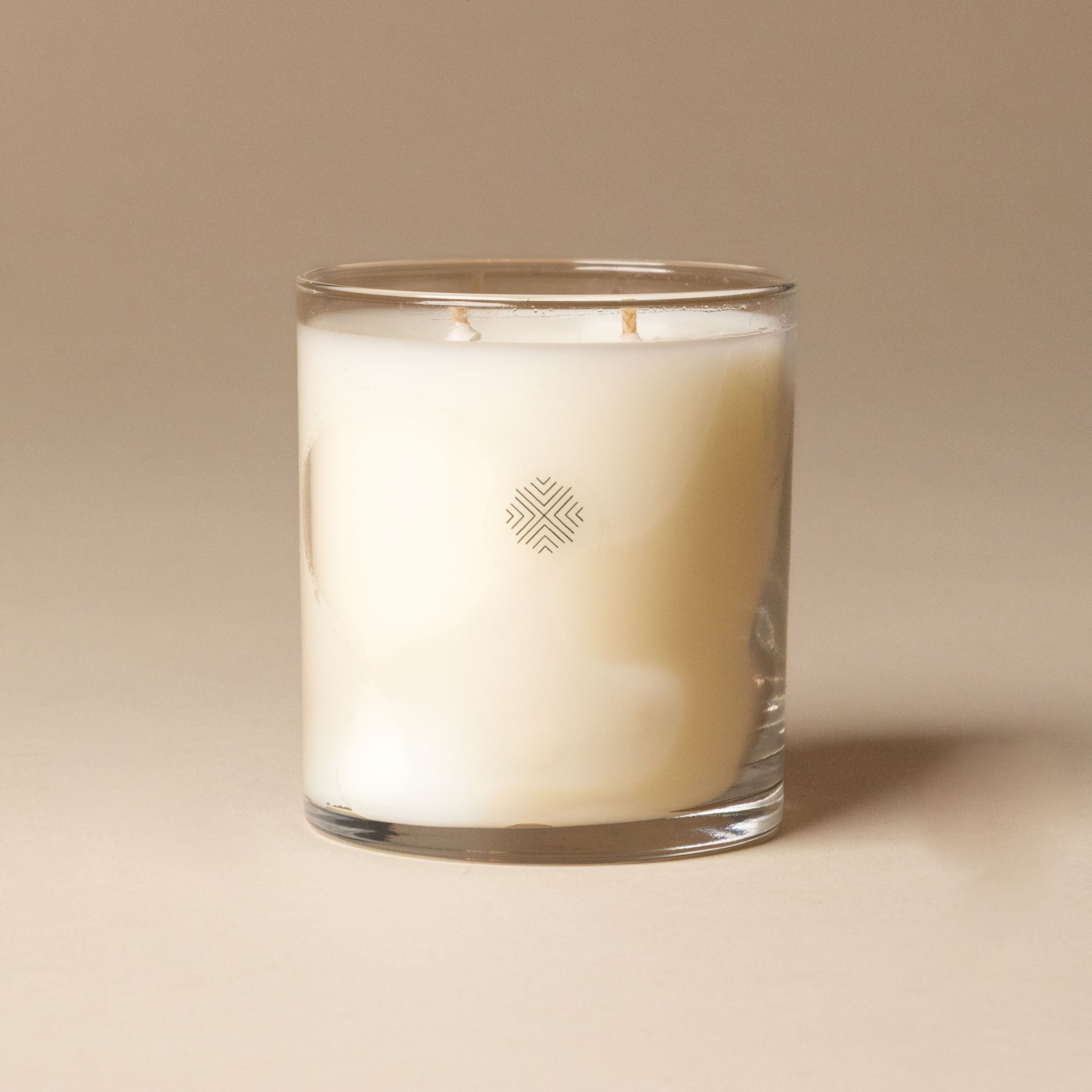 White candle in a glass container with a logo on a beige background