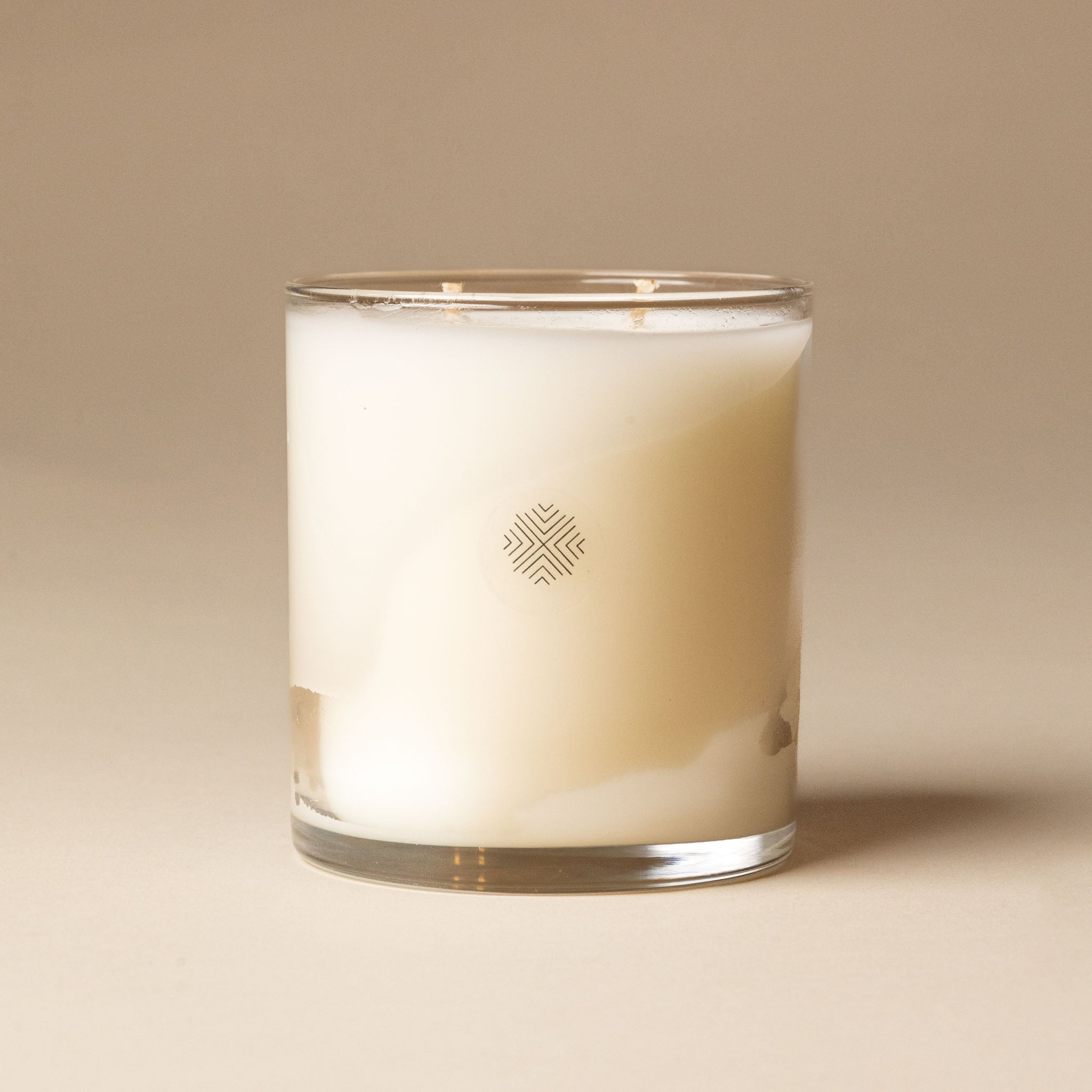 White candle in a glass container with a logo on a beige background