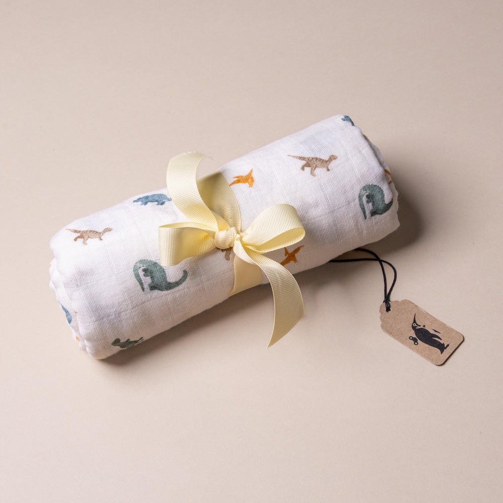 organic-cotton-muslin-swaddle-little-dinos Rolled-up fabric with dinosaur prints and a