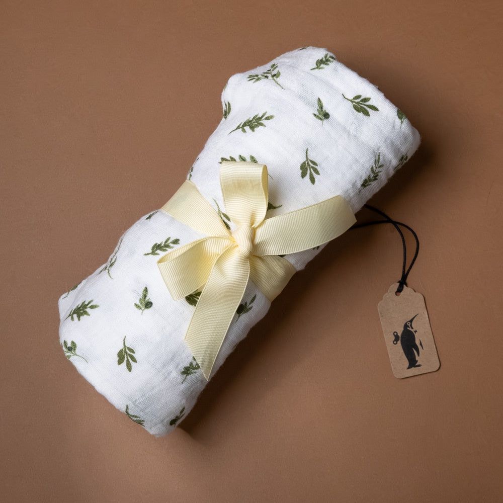 organic-cotton-muslin-swaddle-olive-branch Rolled-up fabric with green leaf pattern and yellow ribbon on a brown background