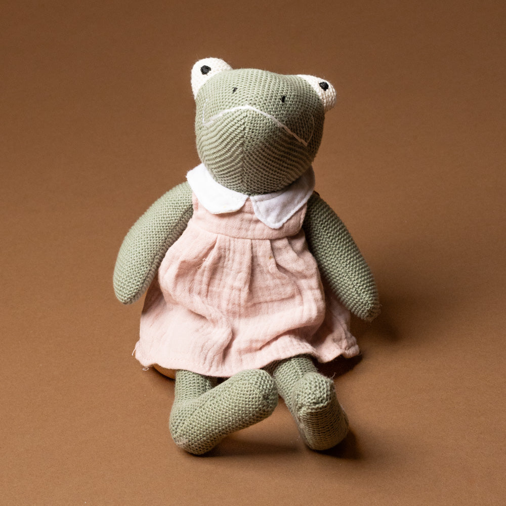 paulette-the-frog-plush-rattle Knitted frog toy wearing a pink dress on a brown background