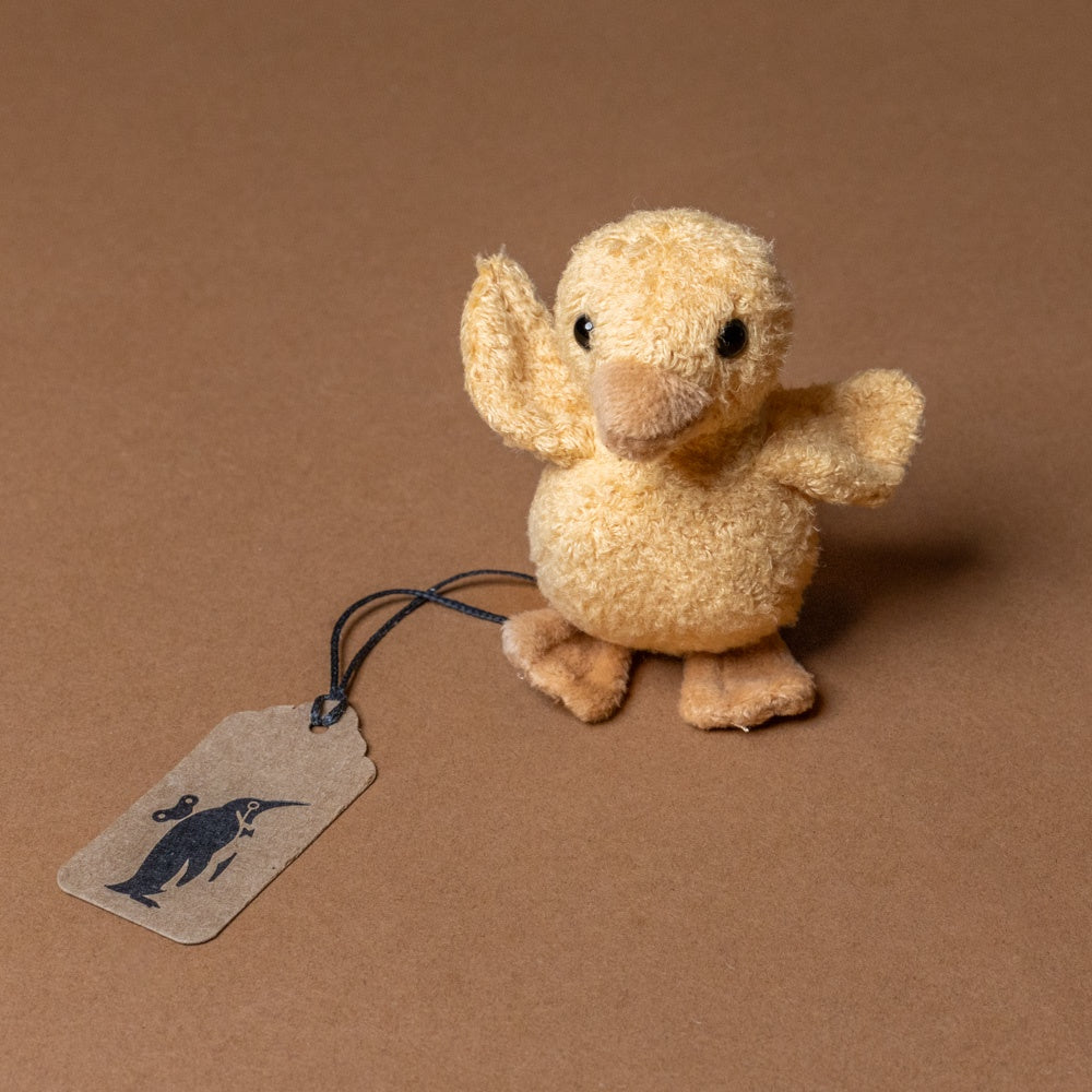quack-the-duckling-awake Small plush duck toy with a tag on a brown background