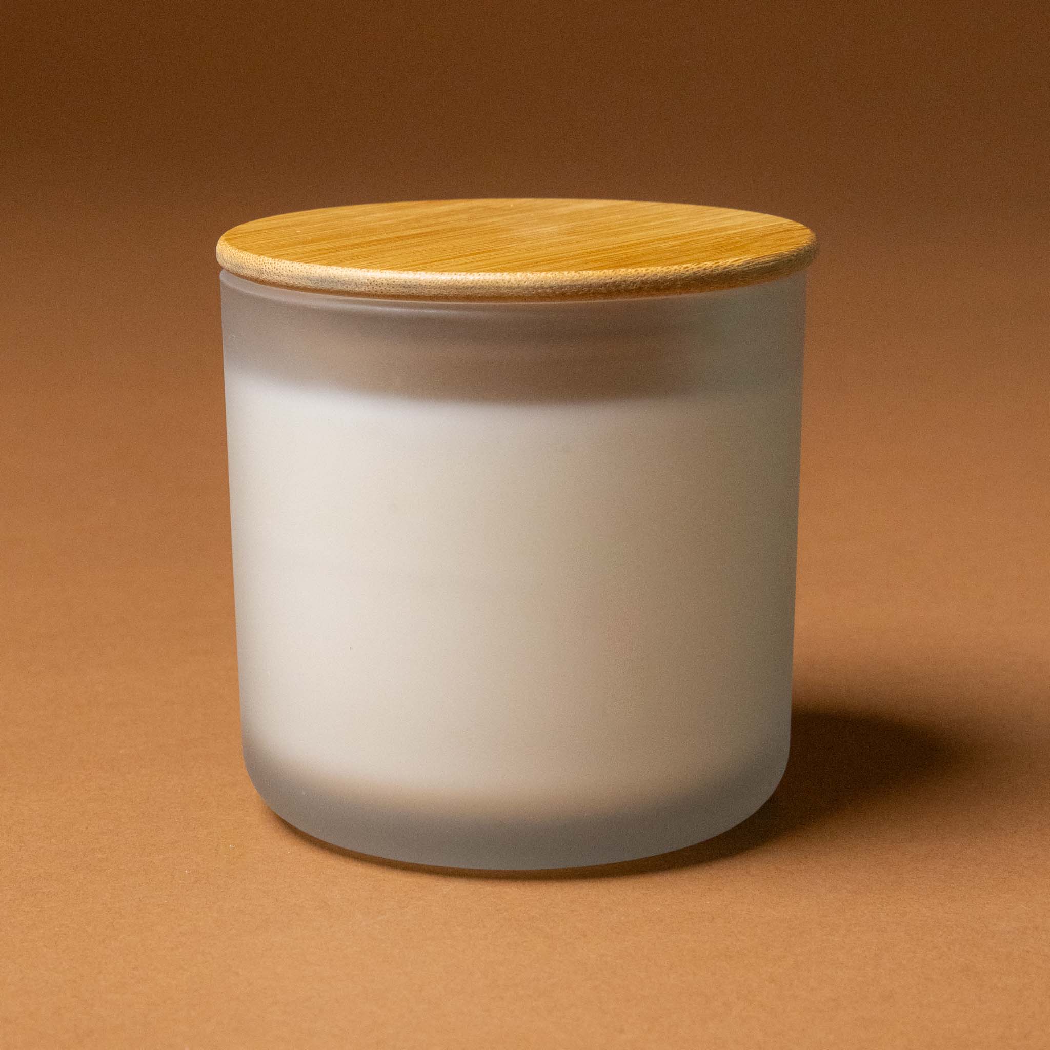 vela-del-jardin-candle-frosted-glass-container with a wooden lid on a brown background