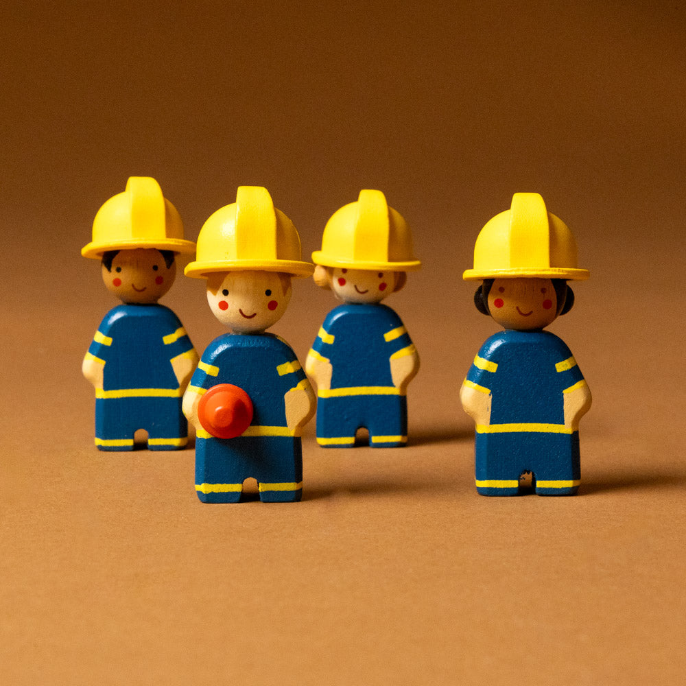 wooden-fire-engine-play-set Four toy figures of firefighters with yellow helmets and blue outfits on a brown background