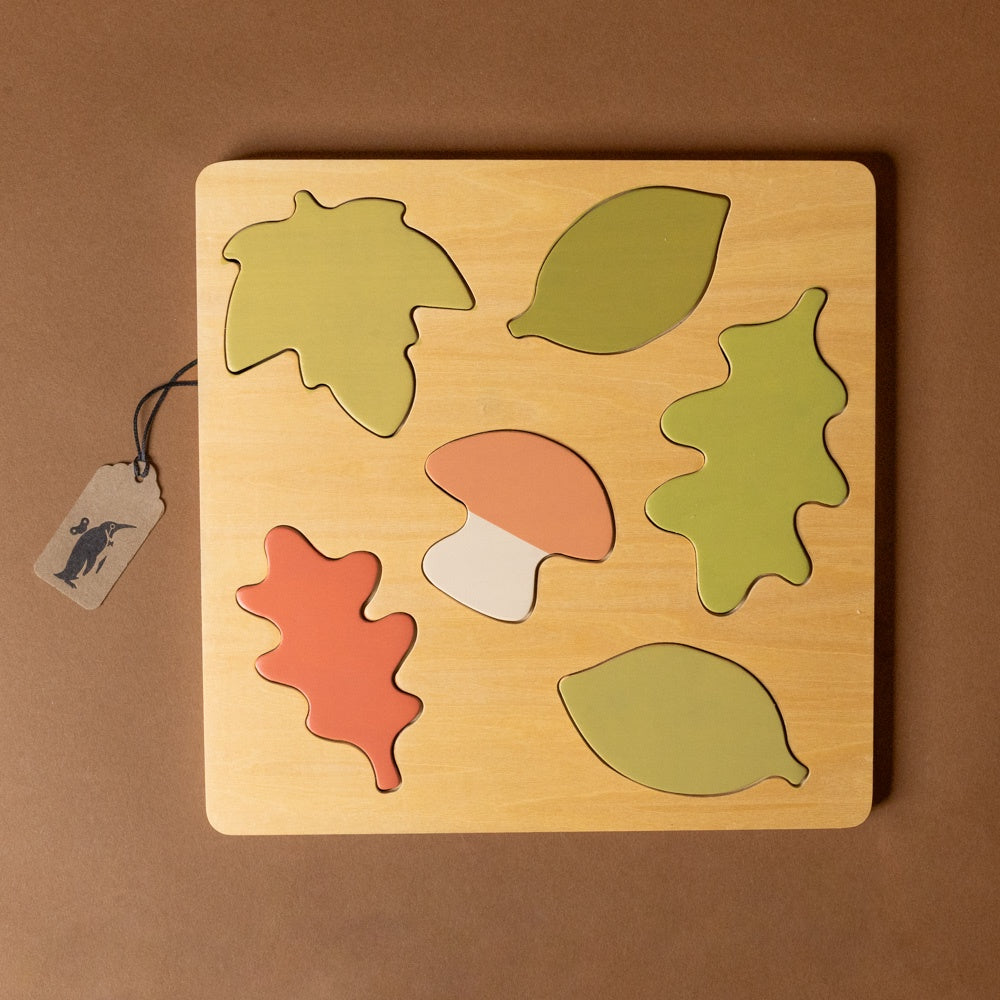 wooden-forest-puzzle Wooden puzzle with leaf and mushroom shapes on a brown background