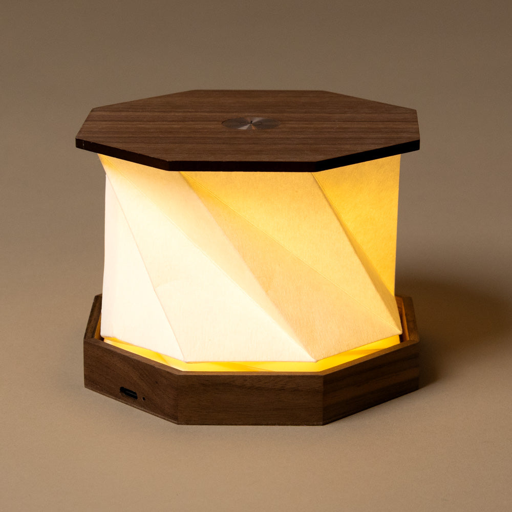 wooden-hexagon-twist-lamp-walnut with a soft glow on a brown background
