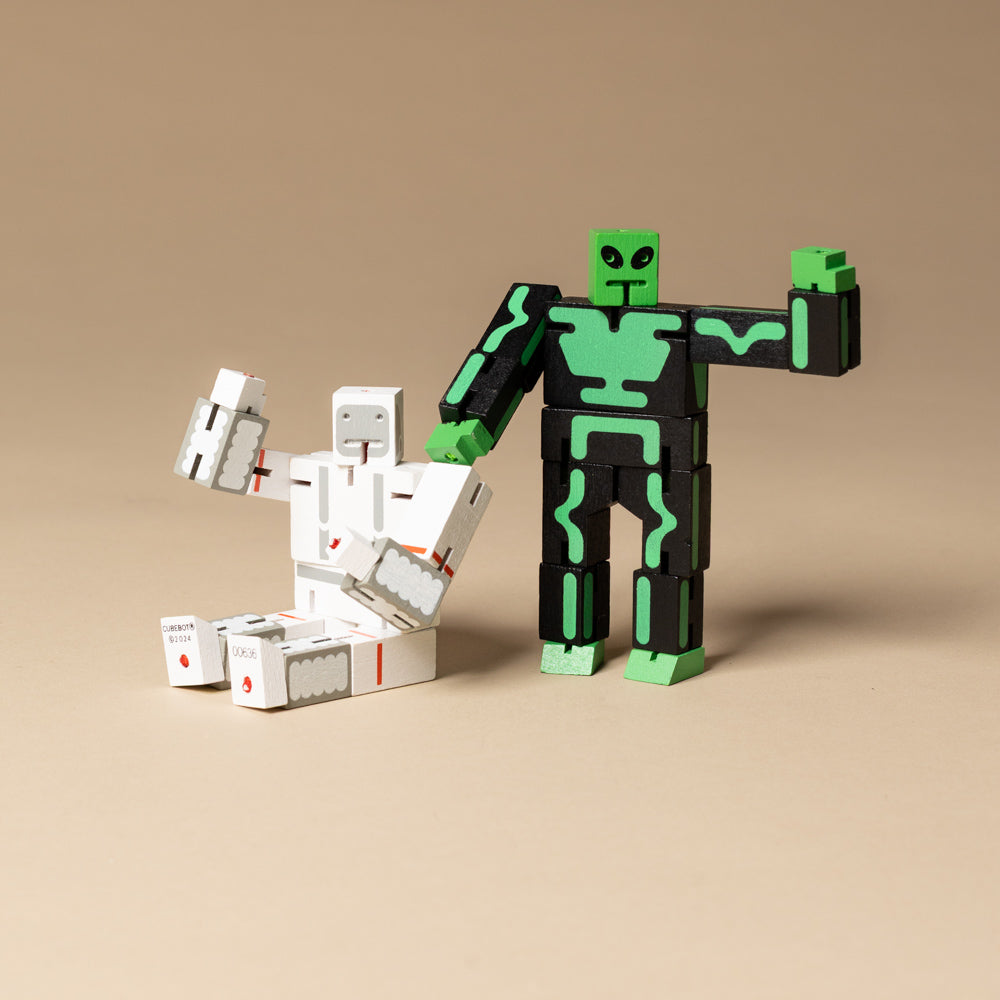 wooden-micro-cubebot-space-buddies-set Two robot toy figures, one black and green and one white with red accents, on a beige background.