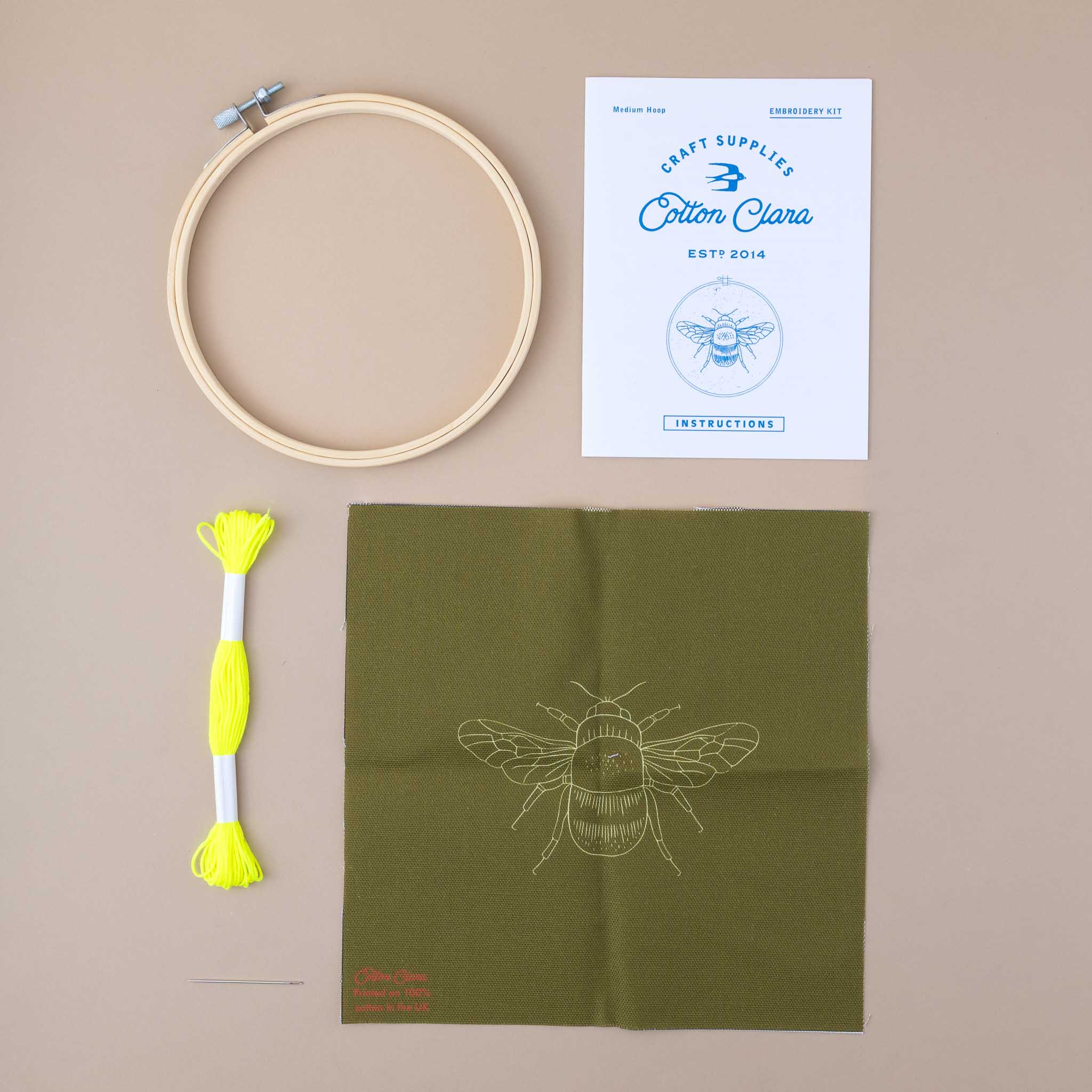 contents of the ebroidery Bee kit showing yellow thread, a loop, the design of the bee on green cloth and the instructions booklet
