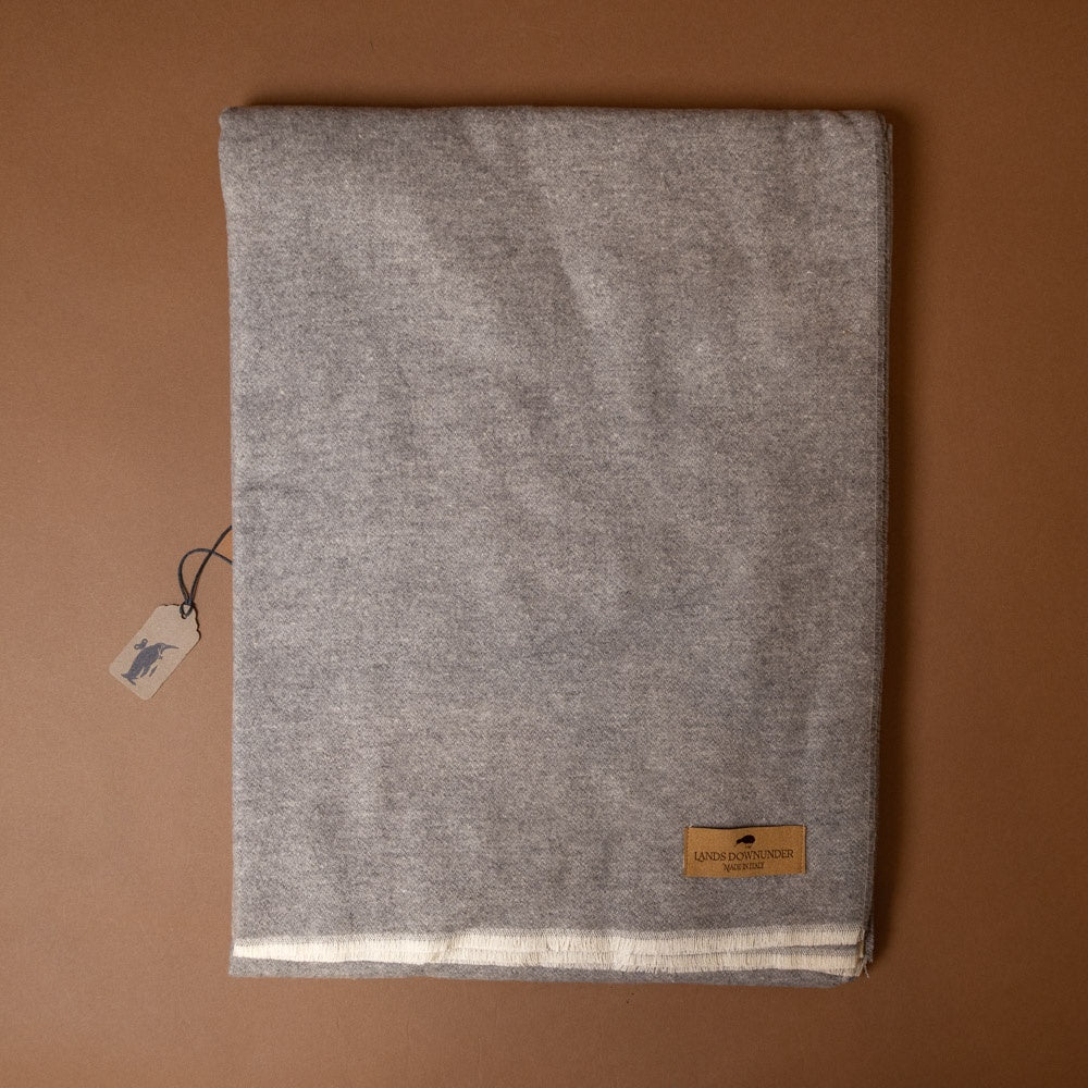 aspen-throw-ash Gray fabric with a brand tag on a brown background