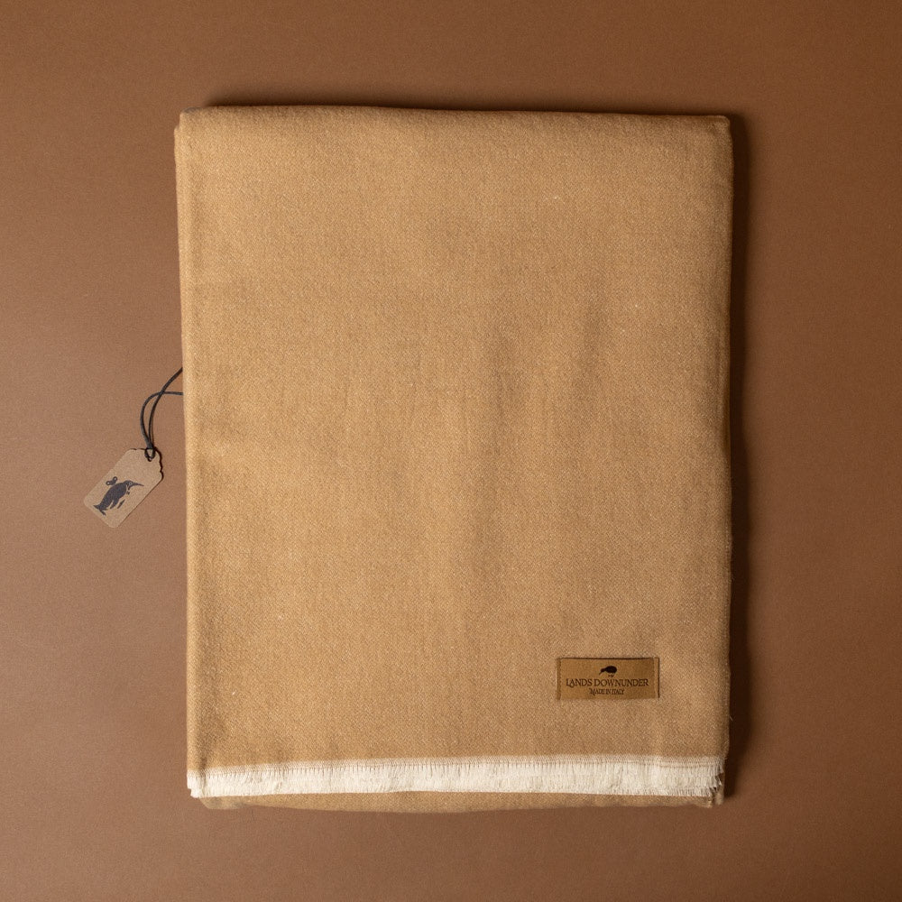 aspen-throw-latte Beige fabric with a tag and label on a brown background