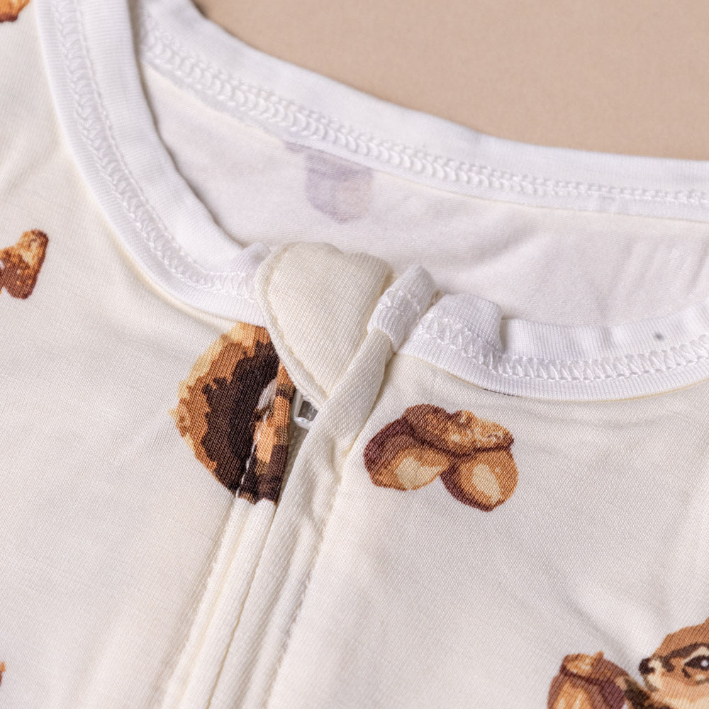 bamboo-stretch-zipper-pajamas-chipmunk Close-up of a baby outfit with acorn pattern and zipper on a beige background