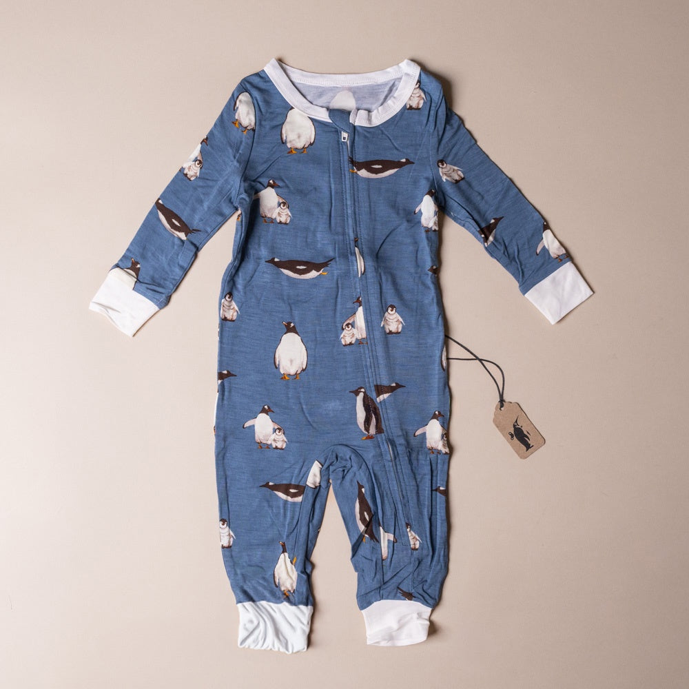 bamboo-zipper-pajamas-penguins Blue baby onesie with penguin pattern on a beige background