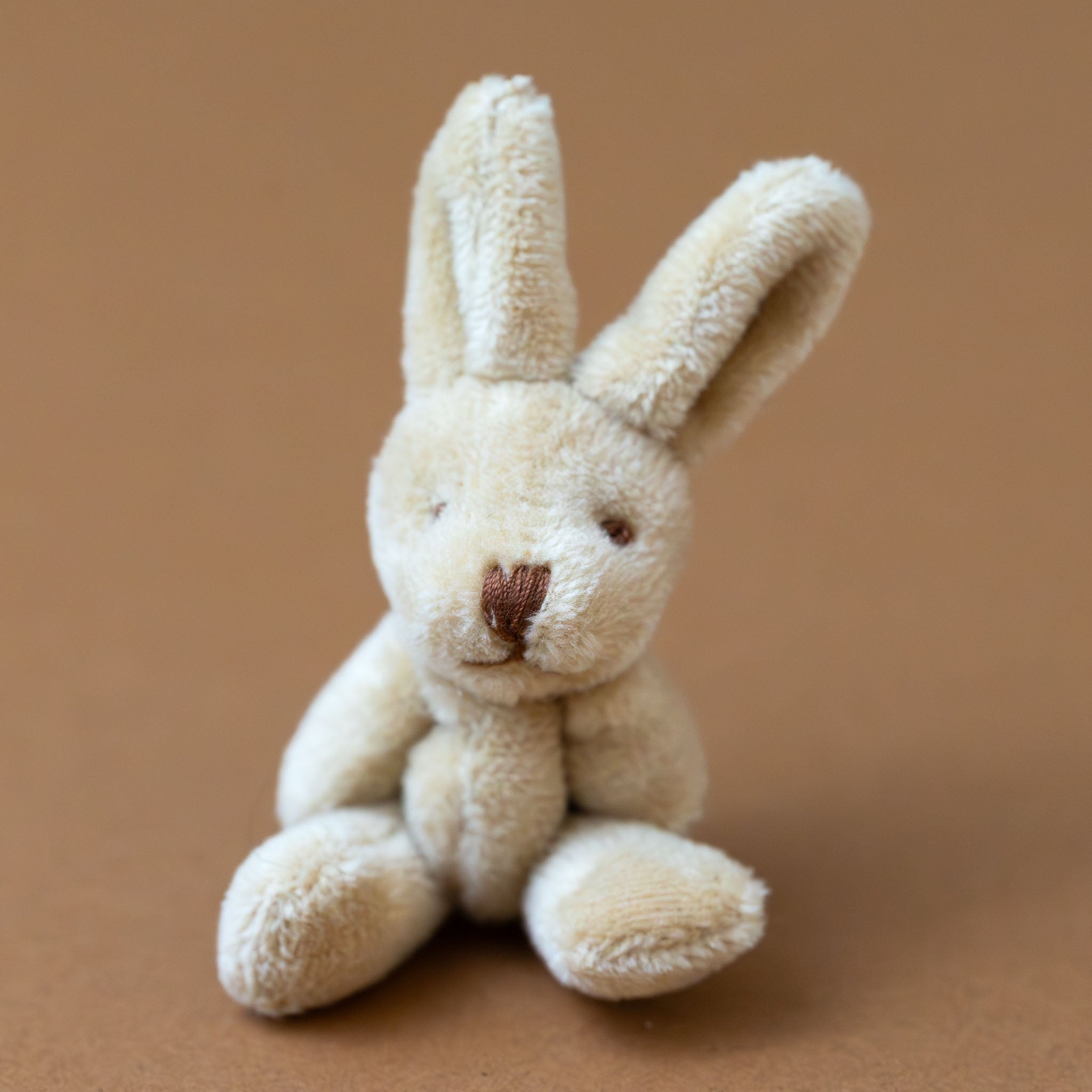 bitty-bunny-oatmeal Small beige stuffed rabbit toy on a brown background