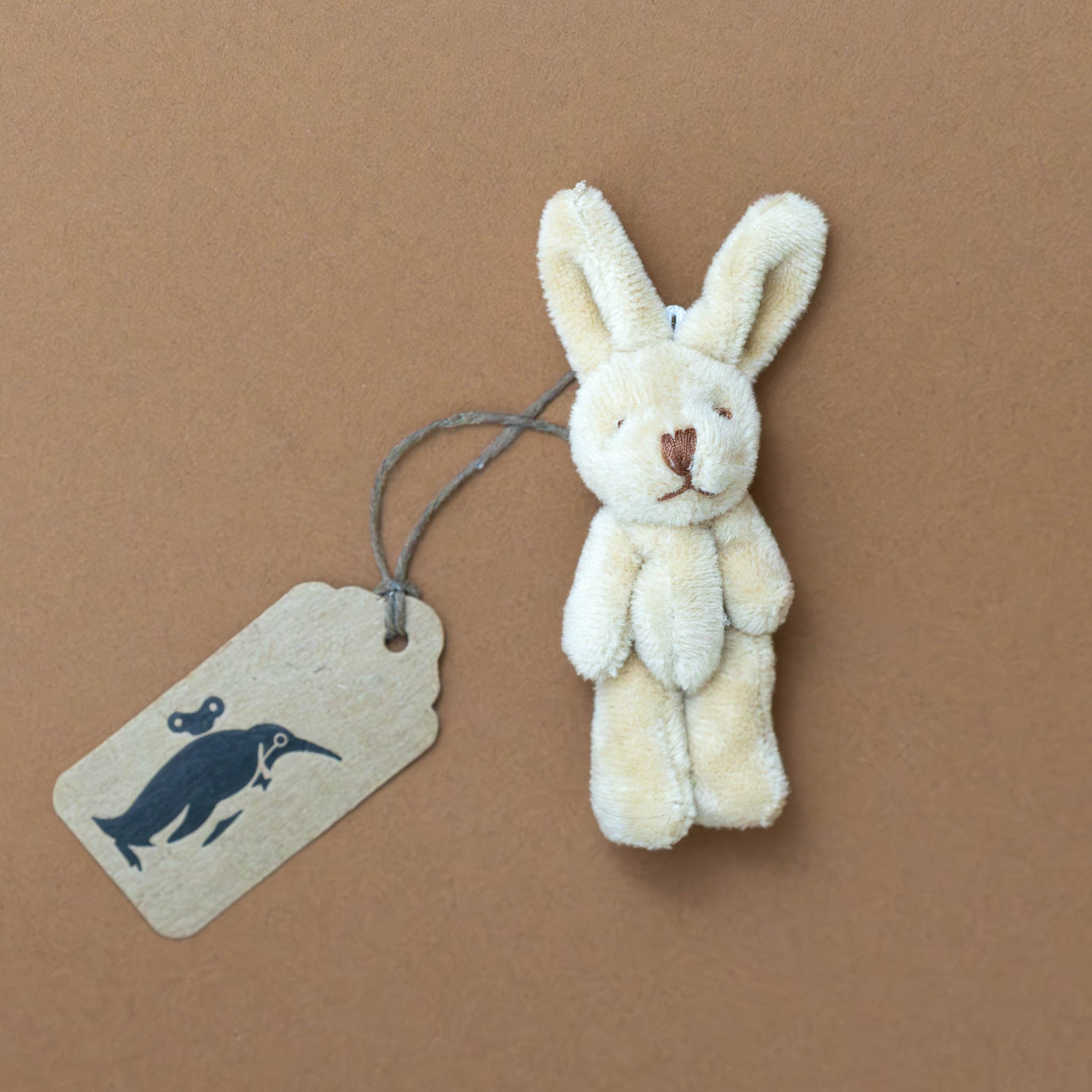 bitty-bunny-oatmeal Small plush bunny toy with a tag on a brown background