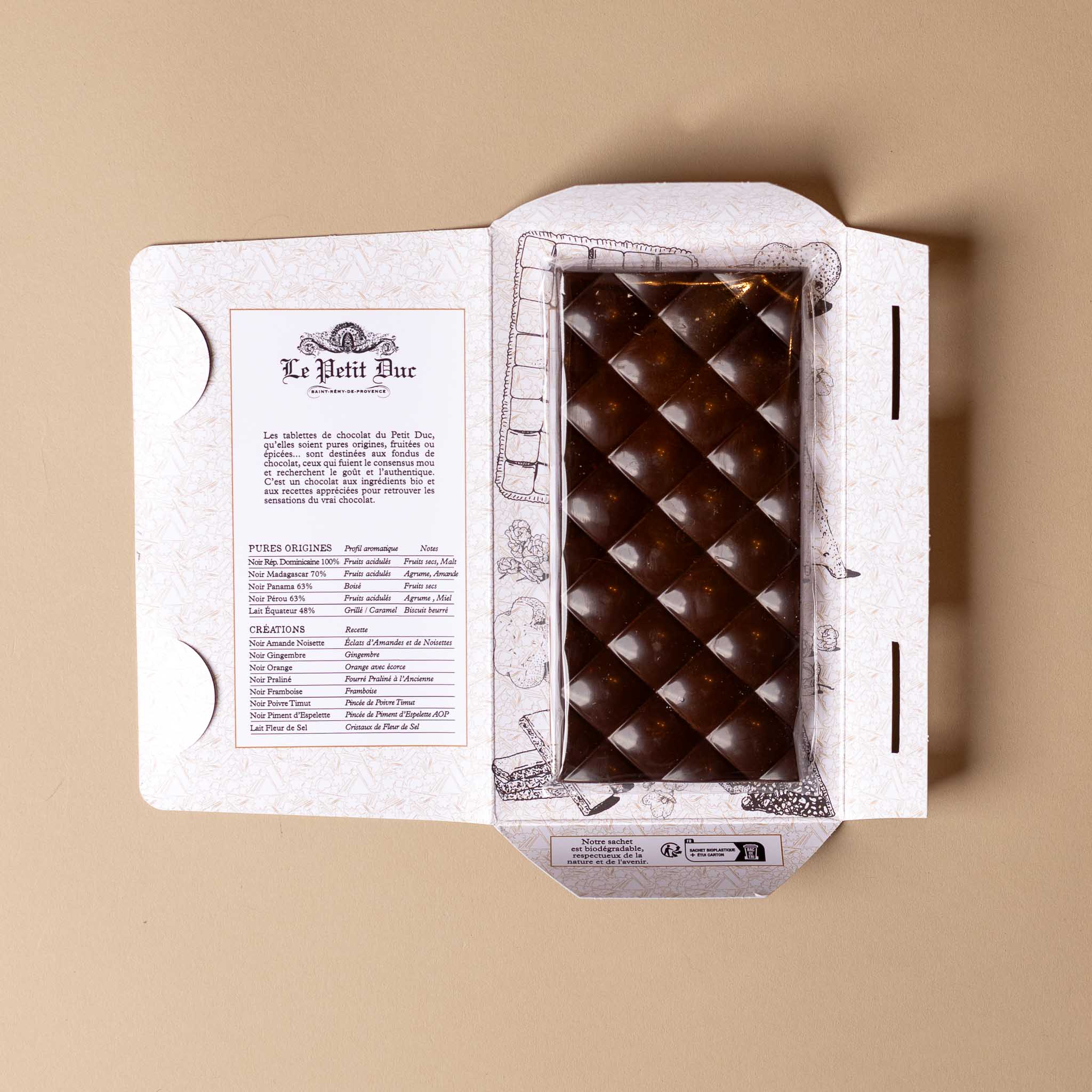 chocolat-noir-bar-espelette-pepper Open box of chocolate bars with a visible brand name on a beige background