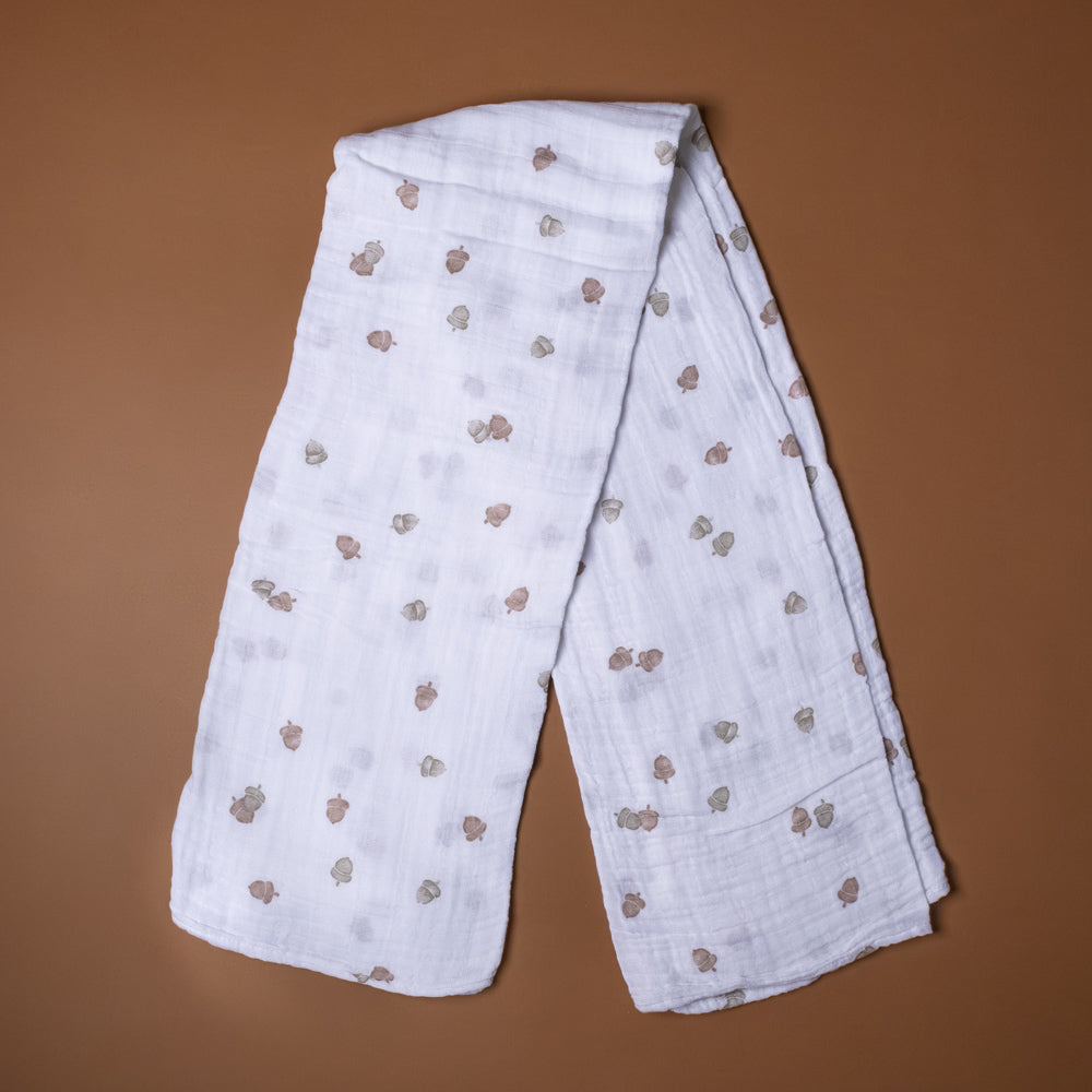 cotton-muslin-swaddle-acorns White fabric with brown acorn patterns on a brown background
