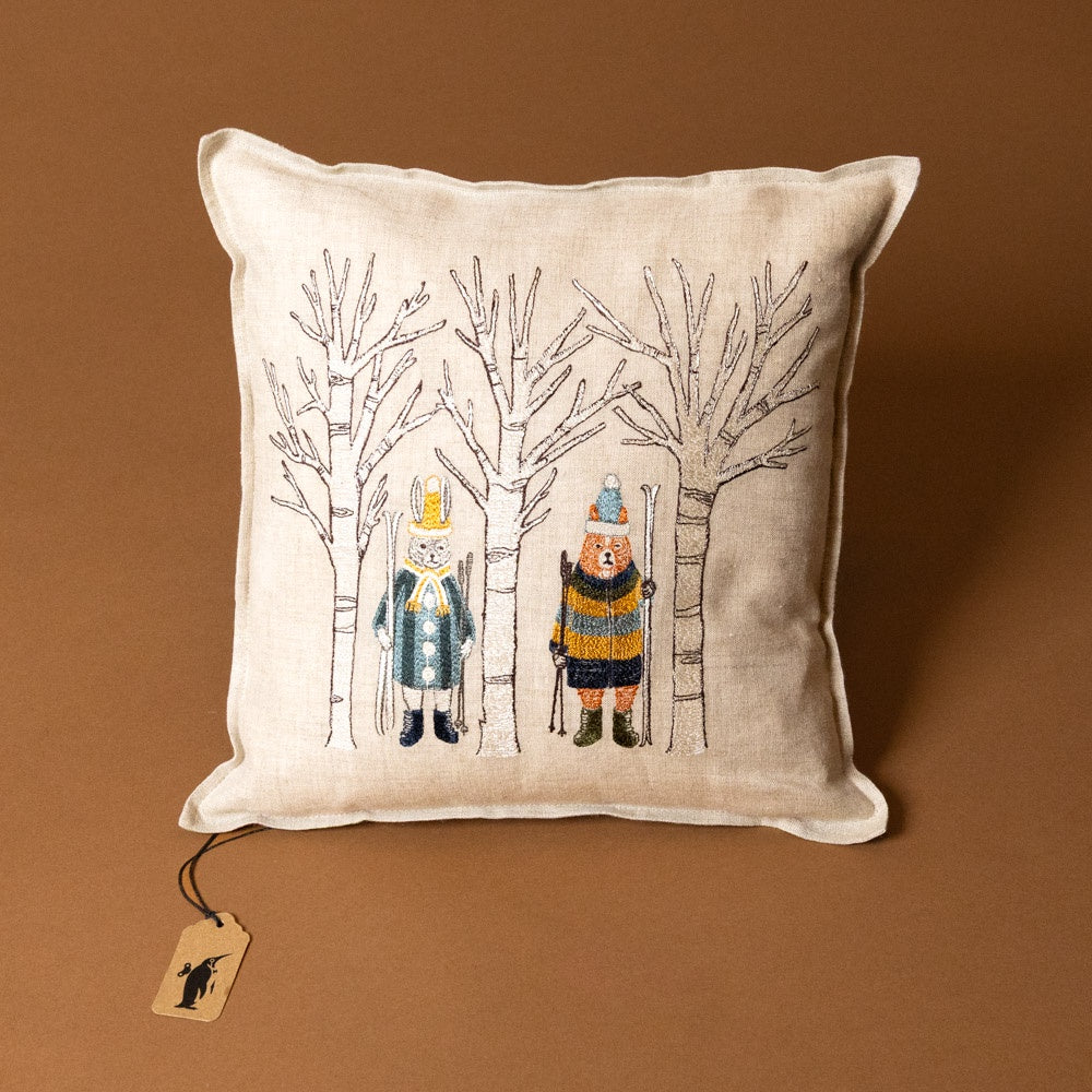 embroidered-pillow-aspen-skiers with winter-themed illustration of characters in the woods on a brown background