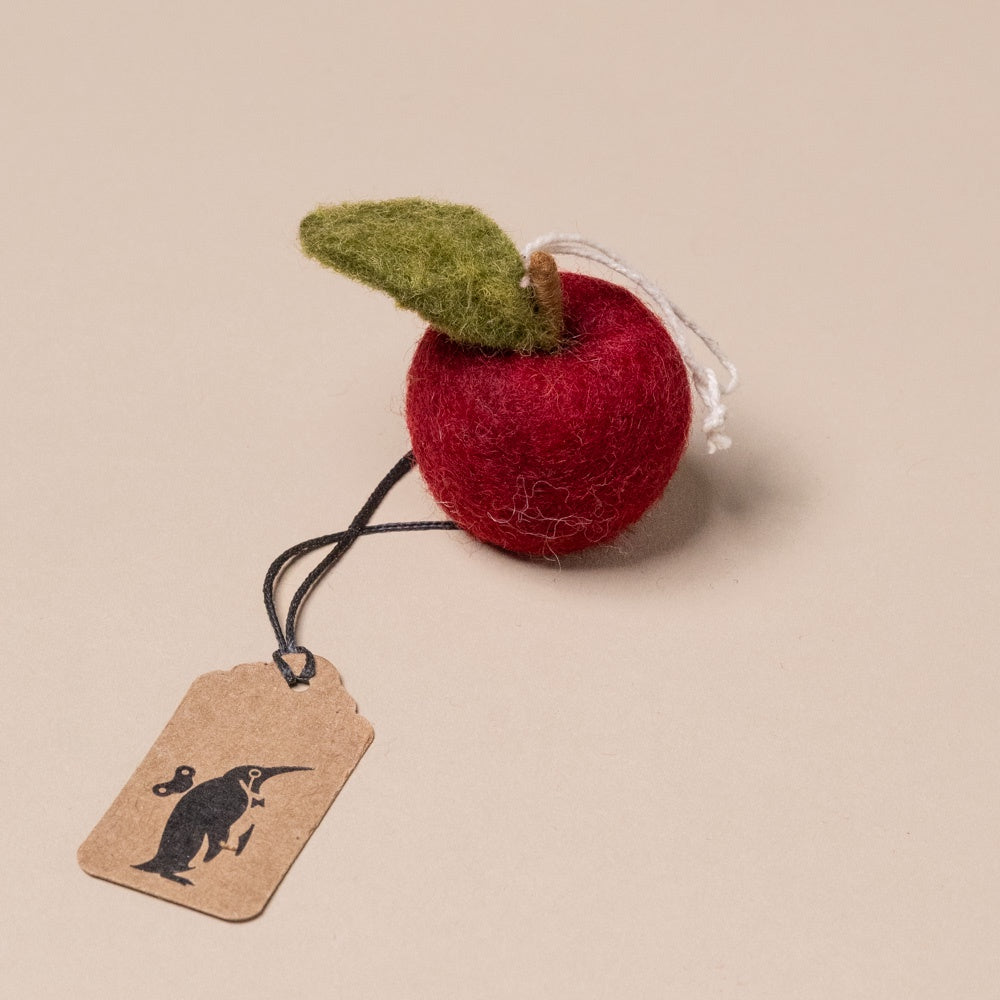 felted-apple-ornament-ruby-red Felted red apple ornament with a green leaf on a beige background
