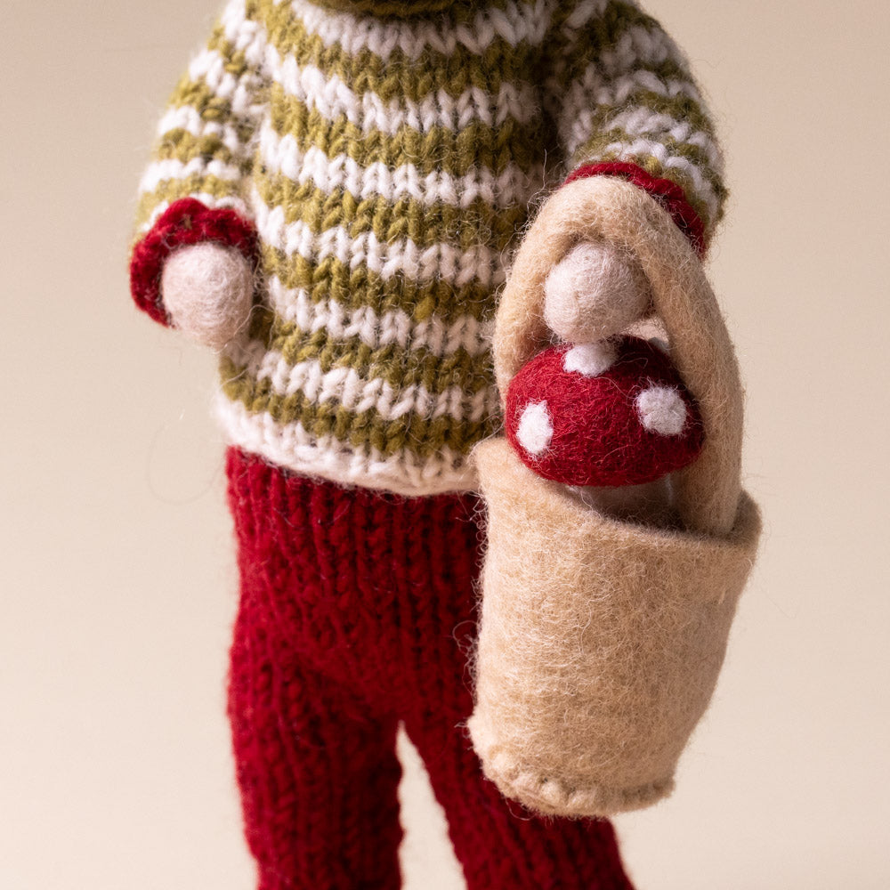felted-grey-mouse-green-striped-sweater-with-mushroom-bucket Knitted outfit with a green and white patterned sweater and red pants, holding a brown bag with a red mushroom.